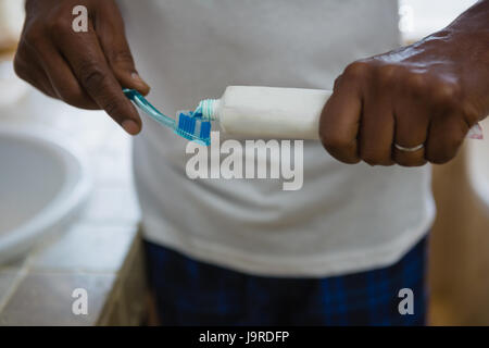 La sezione centrale dell'uomo applicando una pasta dentifricia sulla spazzola in bagno a casa Foto Stock