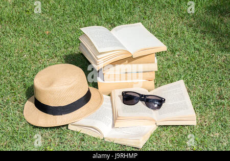 Cappello, occhiali da sole e libri aperti al di fuori di erba Foto Stock