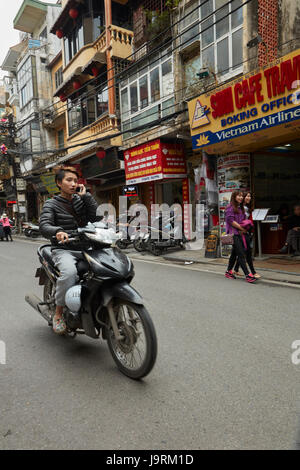 Persona sul cellulare in sella scooter, il vecchio quartiere di Hanoi, Vietnam Foto Stock