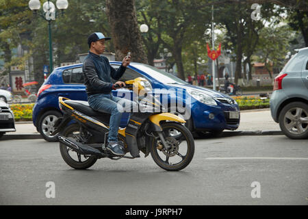 L'uomo sul cellulare in sella scooter, il vecchio quartiere di Hanoi, Vietnam Foto Stock