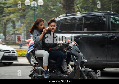 Coppia con bambini su scooter tramite telefono cellulare, il vecchio quartiere di Hanoi, Vietnam Foto Stock