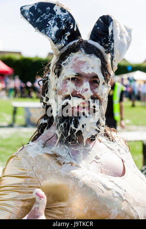 Inghilterra, Coxheath. Cinquantesimo mondo Tortino di crema campionato. Uomo vestito come Bunny girl, volto ricoperto di crema pasticcera, sorridente al visualizzatore. Contatto visivo. Testa e spalle. Foto Stock