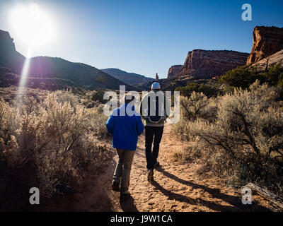 Padre e figlio escursionismo in Colorado National Monument. Monumento Canyon Trail con il monumento di indipendenza nella distanza nel tardo pomeriggio Foto Stock