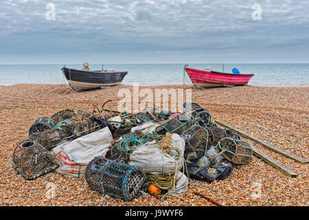 A Bognor Regis beach un mucchio di attrezzi da pesca è in primo piano, due piccole barche da pesca in background sotto un buio, cielo nuvoloso. Foto Stock