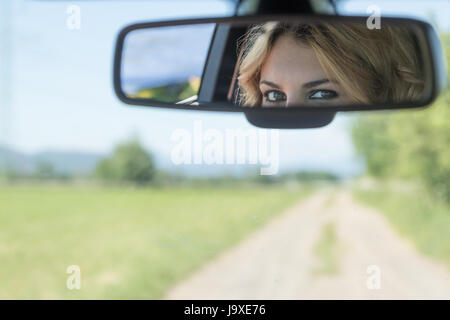 La bella occhi del giovane conducente donna sono riflessi nello specchietto retrovisore. Strada sfocata e il paesaggio è in background. Foto Stock