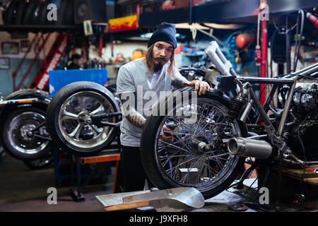 Ritratto di barbuti tatuati uomo che lavora in sintonia di garage per moto e guardando la fotocamera Foto Stock