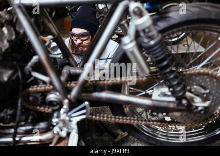 Ritratto di brutale uomo barbuto assemblaggio motociclo personalizzato in garage Foto Stock