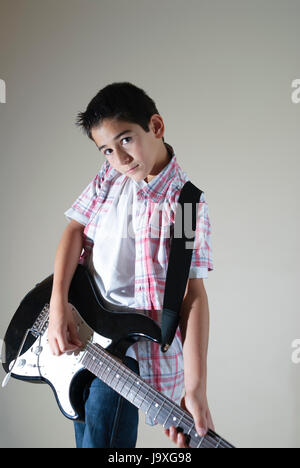 Ragazzo con una chitarra elettrica, isolata sul grigio, che sogna la fama di rockstar, catturando ambizioni giovanili e sogni musicali Foto Stock