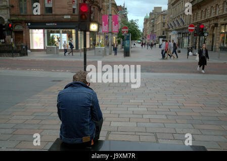 Ragazzo adolescente seduto da solo in una strada dello shopping di notte Buchanan St, Glasgow Foto Stock