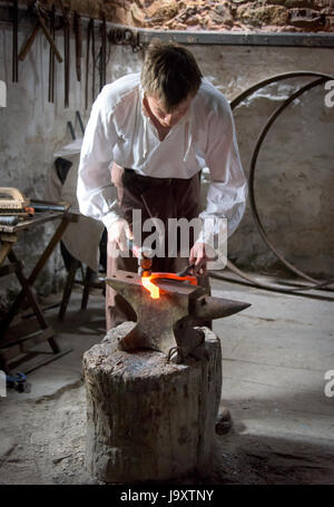 Maniscalco tradizionale messa a ferro di cavallo con un martello e l'incudine e il ferro grezzo metallo, Wales, Regno Unito Foto Stock
