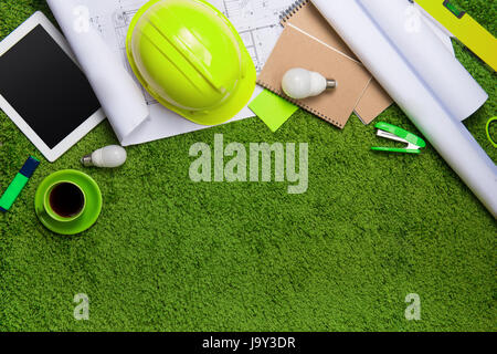 Il luogo di lavoro con casco, blueprint, laptop e blocco note su sfondo di erba. Vista da sopra con lo spazio di copia Foto Stock
