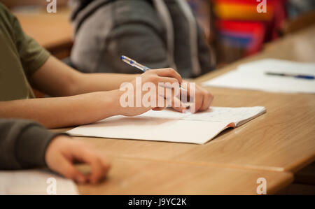 Primo piano dello studente le mani sulla tavola di scuola in classe scrivendo al notebook. L apprendimento, l istruzione e il concetto di scuola Foto Stock