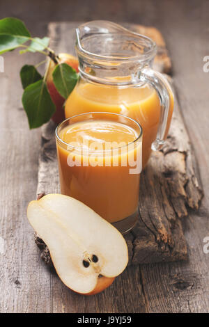 Succhi di pera in un bicchiere di vetro e la brocca, pere fresche su un vecchio sfondo di legno Foto Stock