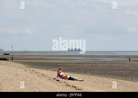 Bagni di sole con navi portacontainer sullo sfondo, a Southend on Sea, Essex, sull'estuario del Tamigi. Spiaggia e litorale Foto Stock