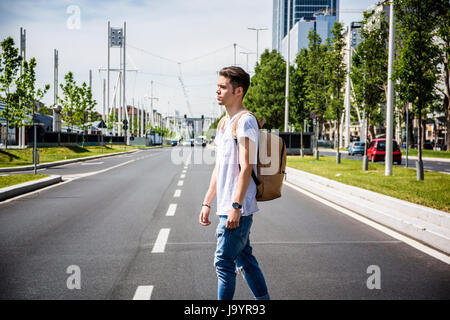 Attraente uomo sorridente in piedi nel centro della città di strada guardando dritto, con zaino Foto Stock