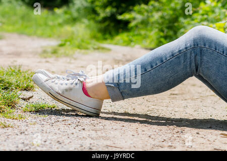 La donna per le gambe in jeans blu e bianco sneakers in tela, in appoggio su una strada sterrata Foto Stock