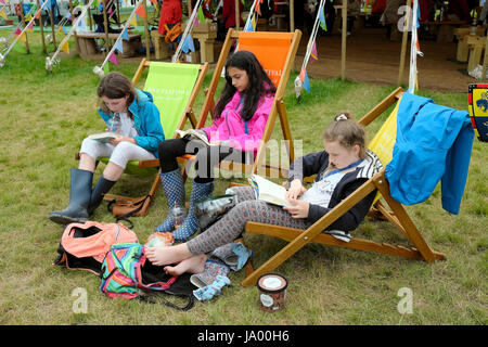 Un gruppo di ragazzi ragazze amici leggere libri seduti su sedie a sdraio presso il Festival di fieno, Hay-on-Wye, Wales UK KATHY DEWITT Foto Stock