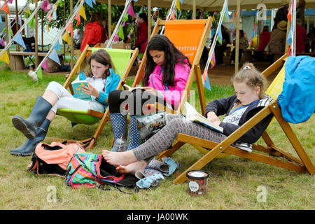 Un gruppo di ragazzi ragazze amici leggere libri seduti su sedie a sdraio presso il Festival di fieno, Hay-on-Wye, Wales UK KATHY DEWITT Foto Stock