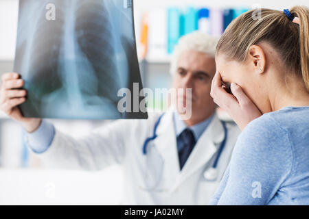 Triste donna avente una consultazione all'ufficio del medico, il medico sta esaminando un x-ray e dando la sua cattiva notizia, il concetto di assistenza sanitaria Foto Stock