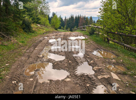 Paese rotto su strada sterrata in primavera montagne con un sacco di pozzanghere fangose dopo la pioggia Foto Stock