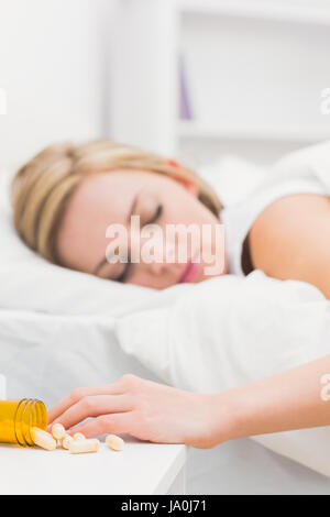 Giovane donna che dorme nel letto con focus sulla fuoriuscita di bottiglia di pillole a casa Foto Stock