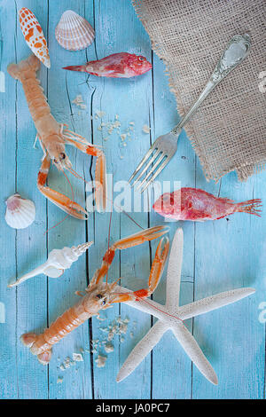 Concetto di mare in tavola: materie aragoste, scorfani e conchiglie blu su sfondo di legno. Foto Stock