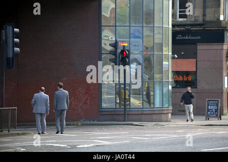 Due uomini in abiti di colore grigio sulla strada al semaforo rosso Charing Cross Glasgow Foto Stock