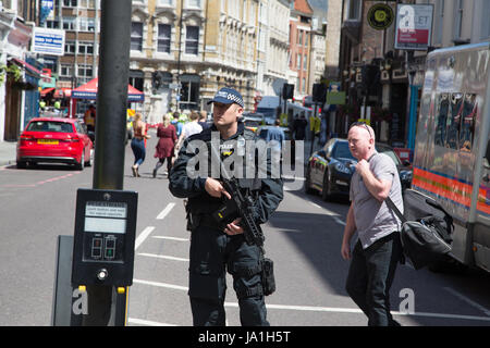 Londra REGNO UNITO. 4 Giugno 2017 Un uomo cammina passato agente di polizia armato in corrispondenza del perimetro cordon, dopo l'ultima notte di terrore di Londra attacco. Theresa Maggio ha lasciato la campagna elettorale sentiero per tenere una riunione di emergenza del comitato di risposta, Cobra, questa mattina a seguito di un attacco terroristico a Londra centrale sabato notte. 7 persone sono state uccise e almeno 48 feriti in attacchi terroristici su London Bridge e di Borough Market. Foto Stock