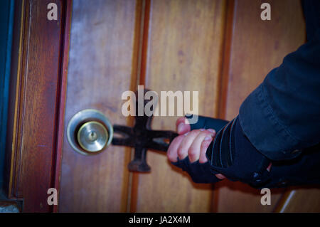 Close up di un ladro con crowbar cercando sfondare la porta per entrare nella casa Foto Stock