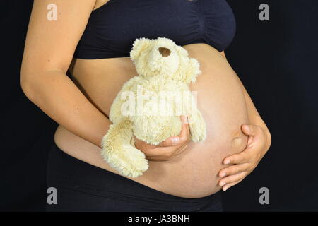 Una donna incinta detiene un simpatico e soffice orsacchiotto contro il lato della sua gobba. Foto Stock