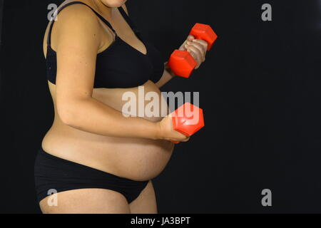 Una donna in stato di gravidanza restare in forma sollevando piccoli pesi rosso Foto Stock