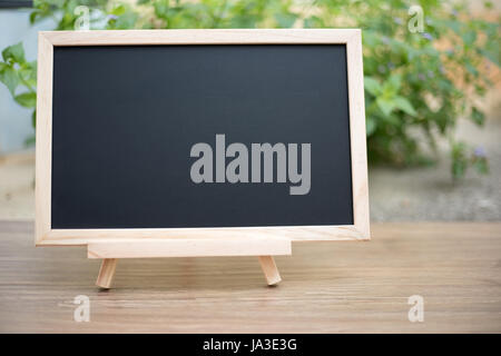 Scheda nero su legno tavolo con Sun e la sfocatura di green tree sfondo bokeh, modello mock up per la visualizzazione del prodotto Foto Stock