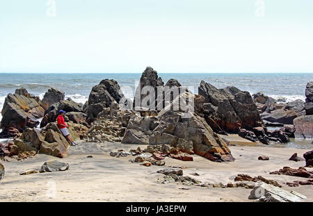 Lone tourist apprezzando il roccioso, pungenti, robusto e tipo di scultura litorale di Arambol Beach in Goa, India Foto Stock