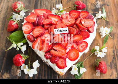 Welcome Card con fragole Cheesecake a forma di cuore in legno rustico sfondo. Foto Stock