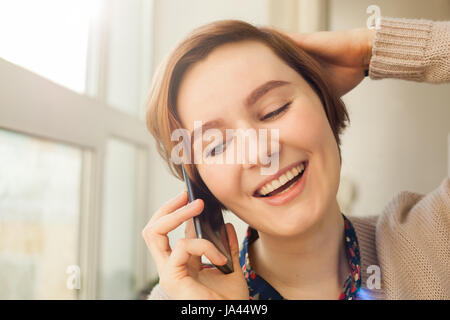 Bellissima ragazza con i capelli corti sognanti con entusiasmo a parlare al telefono Foto Stock