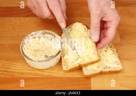 Primo piano delle mani facendo un uovo maionese panino su un tagliere di legno Foto Stock