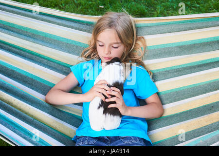 Bambino ragazza bionda seduta o distesa in un amaca e tenendo le sue cavia animale da compagnia. Foto Stock