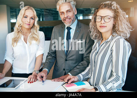 Allegro imprenditori per adulti e due giovani imprenditrici a lavorare con documenti e guardando la fotocamera. Foto Stock