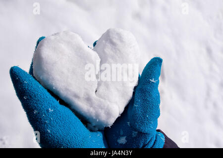 Un uomo in guanti blu contiene neve nelle sue braccia a forma di cuore. Esso è suddiviso in due parti. Simbolo di troncatura e di rottura. Foto Stock