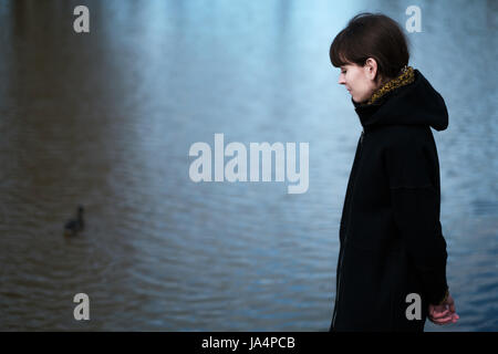 Ritratto di una ragazza solitaria dal lago. Essa si erge vestiti di nero e guarda tristemente a parte, credo circa la cosa triste