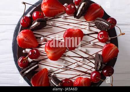 Bella torta al cioccolato con fragola e ciliegia, decorate cookies vicino sul tavolo. vista orizzontale dal di sopra Foto Stock