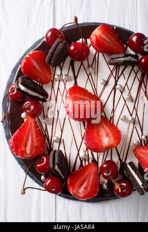 Bella torta al cioccolato con fragola e ciliegia, decorate cookies vicino sul tavolo. vista verticale da sopra Foto Stock