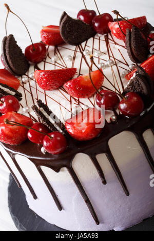 Delicato cheesecake con fragola e ciliegia, decorate biscotti e cioccolata vicino sul piano verticale. Foto Stock