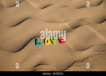 Parola D'AMORE scritta con lettere colorate sulla sabbia soffice del deserto Foto Stock