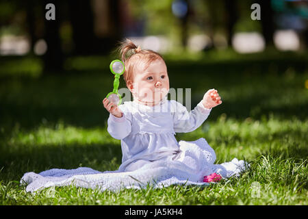 Carino baby ragazza seduta sul prato verde nel parco della città a caldo giorno d'estate. Foto Stock