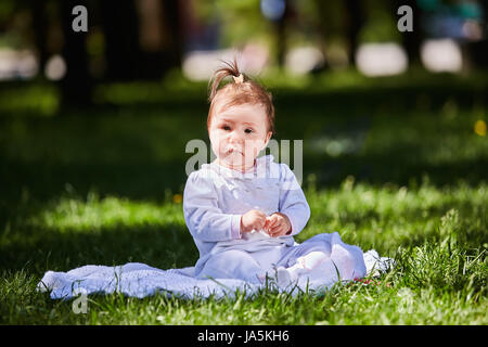 Carino baby ragazza seduta sul prato verde nel parco della città a caldo giorno d'estate. Foto Stock