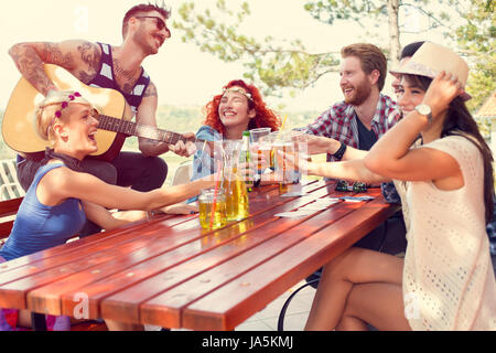 Giovani gioiosi suonare la chitarra e toast con bicchieri di birra in natura Foto Stock