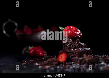 Fragola giacente su una piramide di cioccolato con fette di altre fragole e argento vecchio vaso Foto Stock