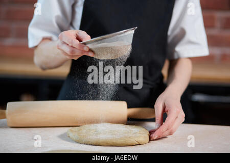 Interni orizzontali crop colpo di cuocere aggiungendo farina per l'impastare su una cucina del ristorante. Irriconoscibile facendo cuocere la pasta. Produrre un impasto Foto Stock