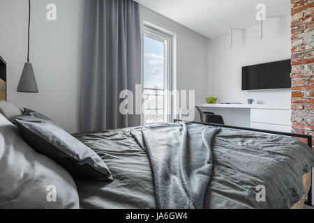 Grigio e bianco camera da letto con un muro di mattoni, letto matrimoniale e tv Foto Stock